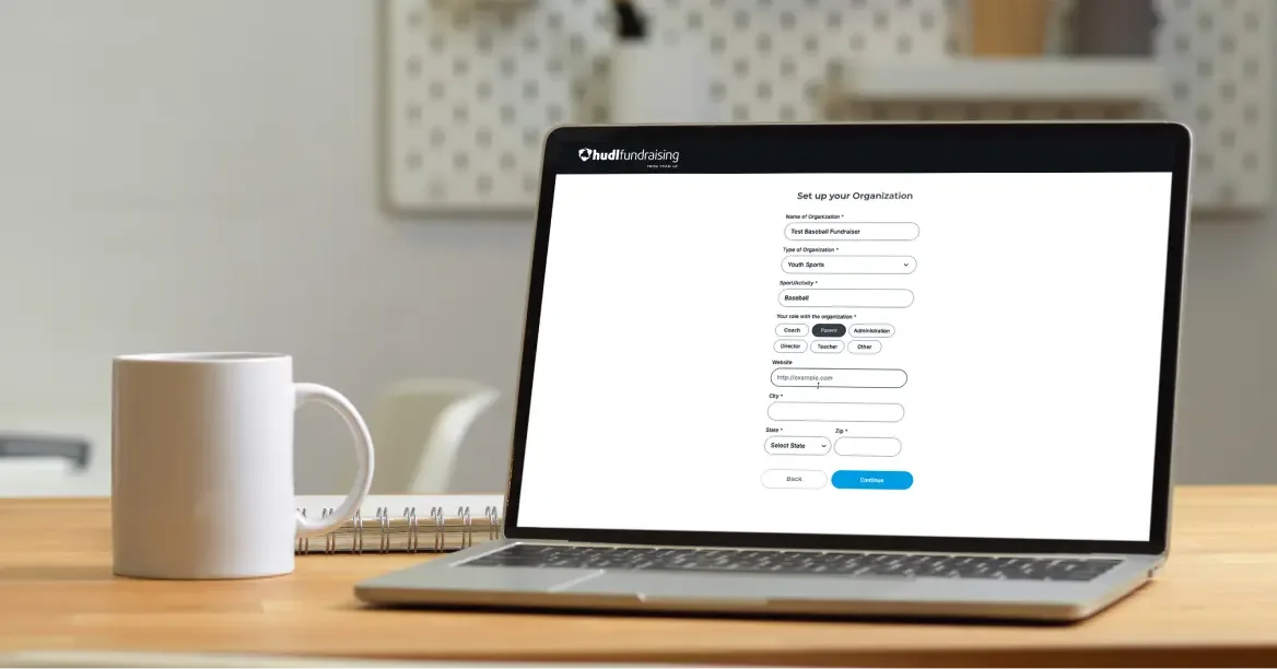A laptop on a table showing a Hudl Fundraising setup form in a browser.